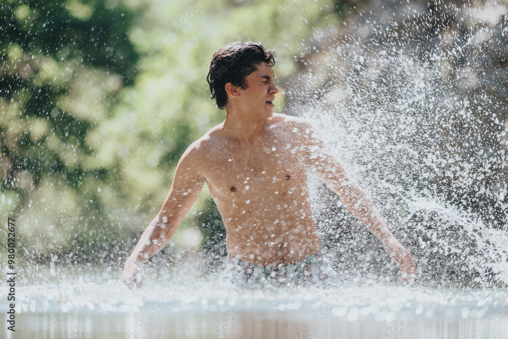 Obraz premium A young shirtless man splashes water playfully in a bright, natural outdoor setting, capturing a moment of joy and refreshment.
