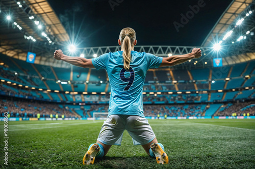 Soccer player in a light blue jersey kneels on the field with arms raised in triumph celebrating a victory under the stadium lights. Back view of a professional football player celebrating a goal photo