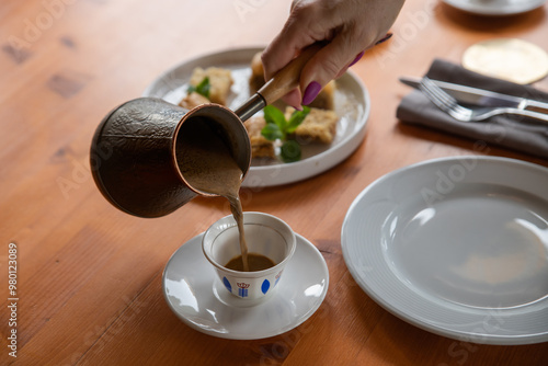 Hot coffee in a cezve. Turkish and Arabic style of making coffee. A woman's hand pours hot coffee into an Arabic cup.Selective focus, close-up.