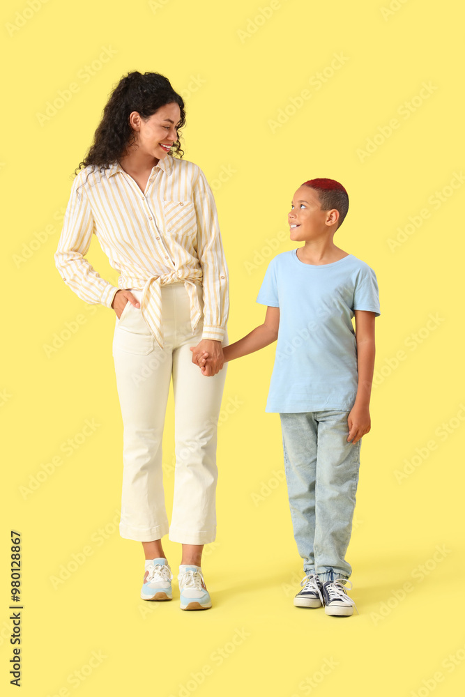 Little African-American boy with his mother holding hands on yellow background Little African-American boy with his mother holding hands on yellow background