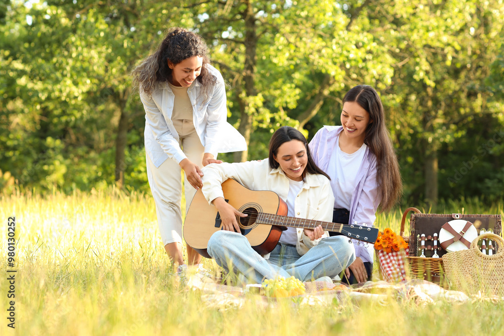 Female friends playing guitar on picnic in park Female friends playing guitar on picnic in park