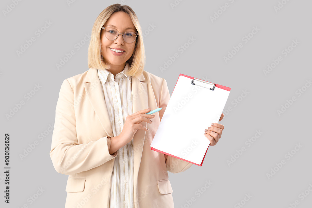 Mature female math teacher with clipboard and pen on grey background Mature female math teacher with clipboard and pen on grey background