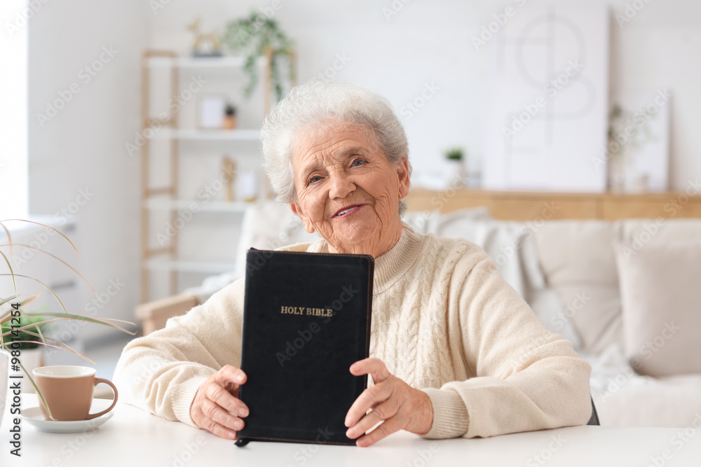 Senior woman with Bible sitting at table in living room Senior woman with Bible sitting at table in living room