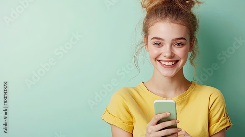 A cheerful young woman smiles while holding a smartphone against a pastel green background, showcasing happiness and connectivity. photo