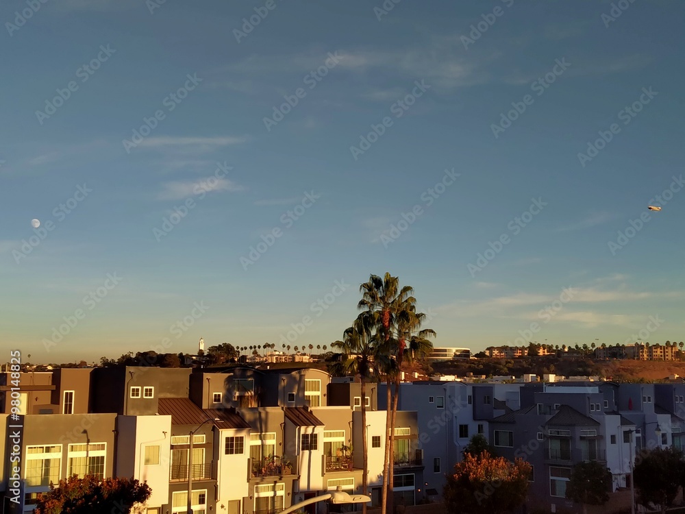 A serene wide shot of Playa Vista at dusk, capturing a tranquil cityscape with the last light of the day casting a soft glow on modern buildings. A row of tall, graceful palms stands on the distant.