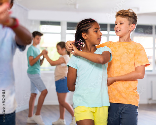 Group of positive juvenile boys and girls doing Tango poses in training room during workout session photo