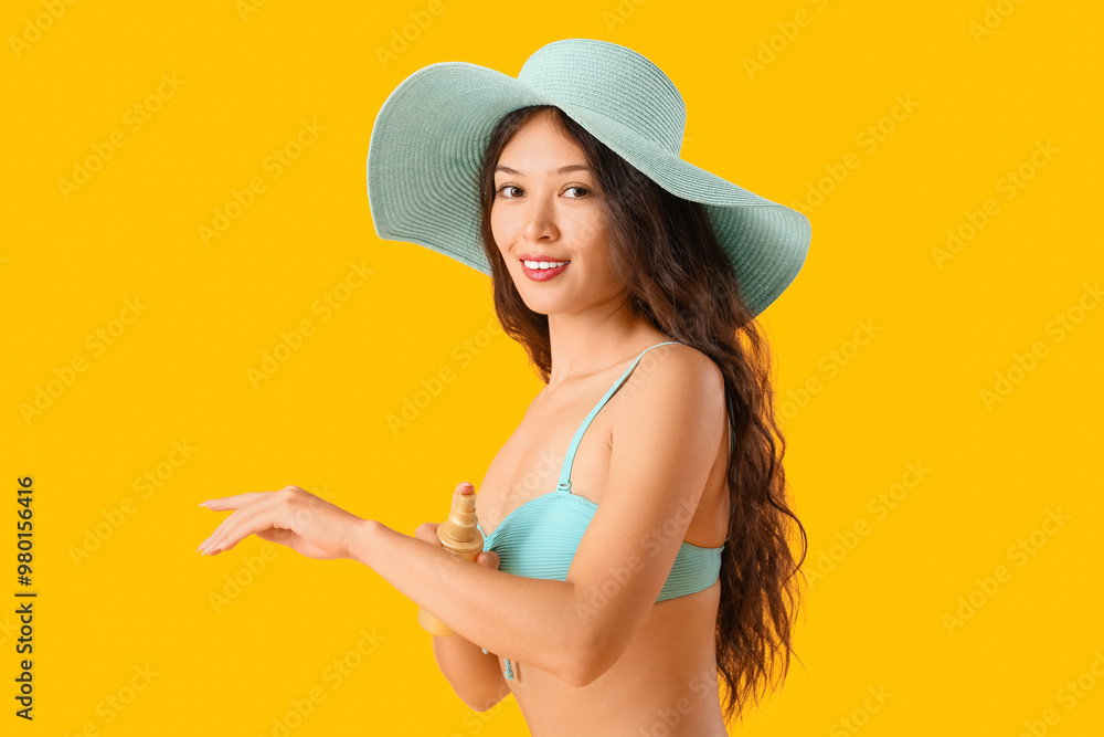 Young Asian woman in swimsuit applying sunscreen cream on yellow background Young Asian woman in swimsuit applying sunscreen cream on yellow background