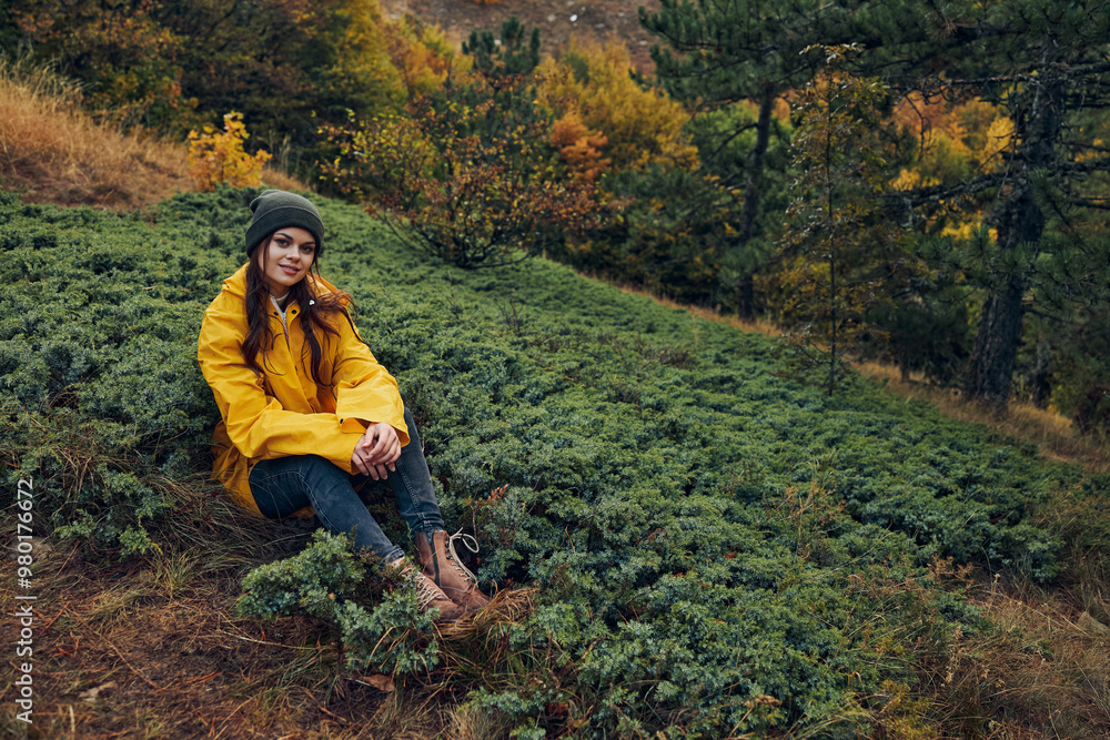 Serene young woman in a vibrant yellow coat enjoying the autumn beauty of a forest hill