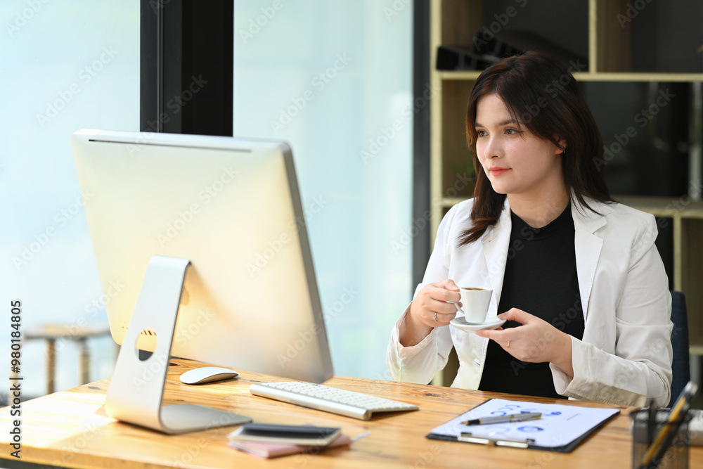 Professional businesswoman dressed in a formal suit drinking coffee and working in modern office Professional businesswoman dressed in a formal suit drinking coffee and working in modern office