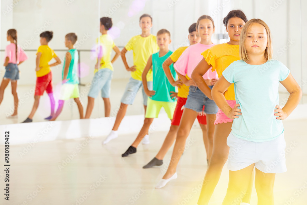 Fototapeta premium Group of positive children rehearsing movements of ballet in classroom