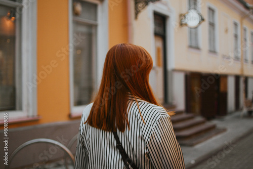 a woman with red hair walks along a street with bars and restaurants in a European city