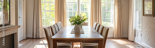 A bright dining room with a wooden table, chairs, and a floral centerpiece by large windows.