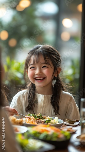 A young girl smiles brightly while enjoying a meal at a restaurant.