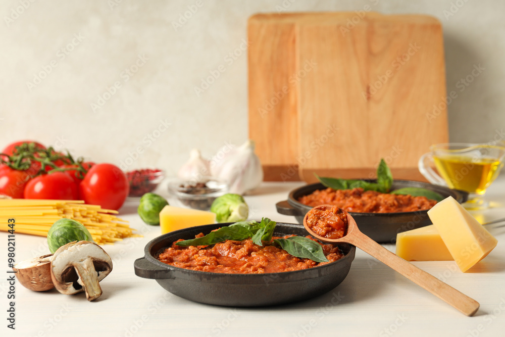 Pans with Bolognese sauce, wooden spoon and ingredients on light background Pans with Bolognese sauce, wooden spoon and ingredients on light background