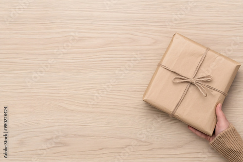 A person is holding a brown box with a string tied around it. The box is wrapped in brown paper and has a bow on top. Concept of anticipation and excitement, as the person is holding the gift