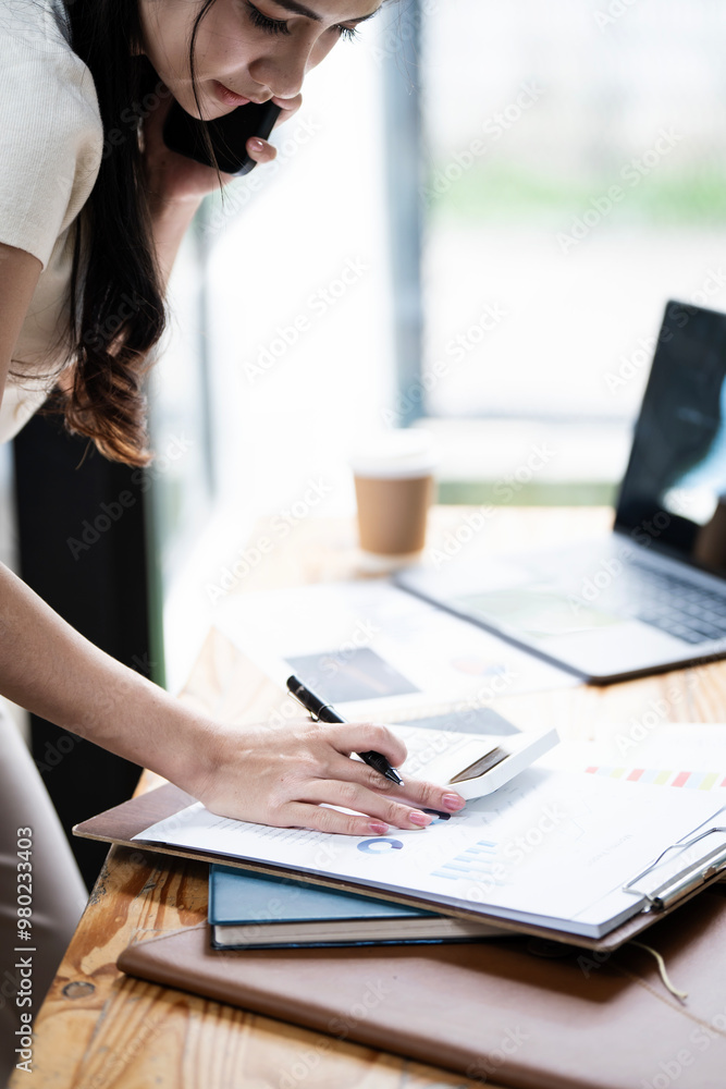 Fototapeta premium Cheerful business Asian woman freelancer making telephone call share good news about project working in office workplace, business finance concept.
