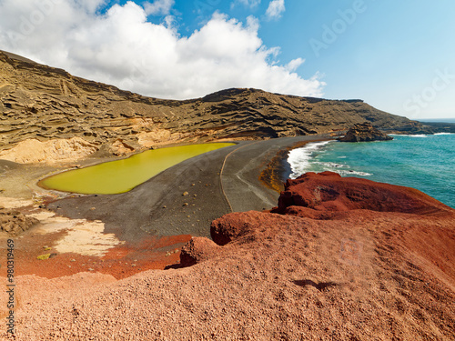 breathtaking aerial view of Charco de los Clicos on Lanzarote. The emerald green lagoon is nestled amidst a colorful volcanic landscape of red cliffs, black sand beaches, and yellow volcanic rocks. 