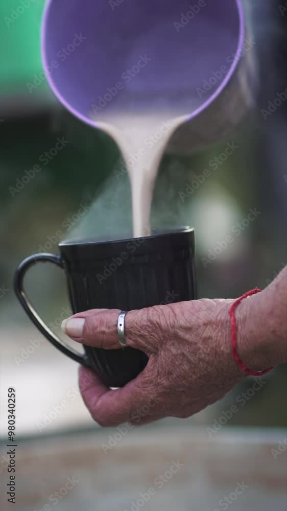 Close up of hot chocolate milk being poured from a purple container into a large mug, with steam rising, suggesting an outdoor cooking scene Close up of hot chocolate milk being poured from a purple container into a large mug, with steam rising, suggesting an outdoor cooking scene