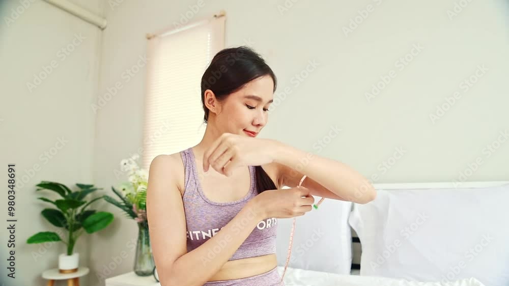 Portrait Asian woman exercising in sportswear using tape measure to measure her arms happy and satisfied with the size of her beautiful, arms, she looks at the camera with cheerful mood. Portrait Asian woman exercising in sportswear using tape measure to measure her arms happy and satisfied with the size of her beautiful, arms, she looks at the camera with cheerful mood.