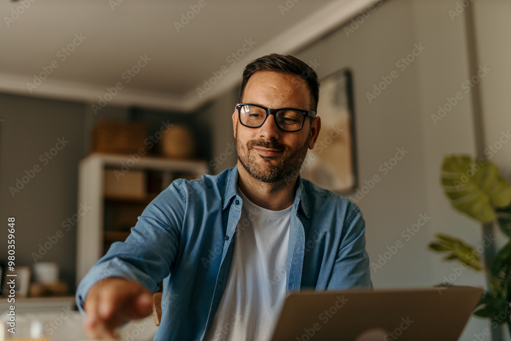 A focused mid aged male freelancer sitting at the wooden table at home and reading online projects on a laptop. A focused mid aged male freelancer sitting at the wooden table at home and reading online projects on a laptop.