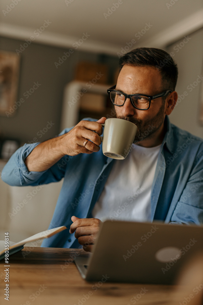 A young Caucasian businessman is working from home and having a cup of coffee as he's sitting at his computer. A young Caucasian businessman is working from home and having a cup of coffee as he's sitting at his computer.