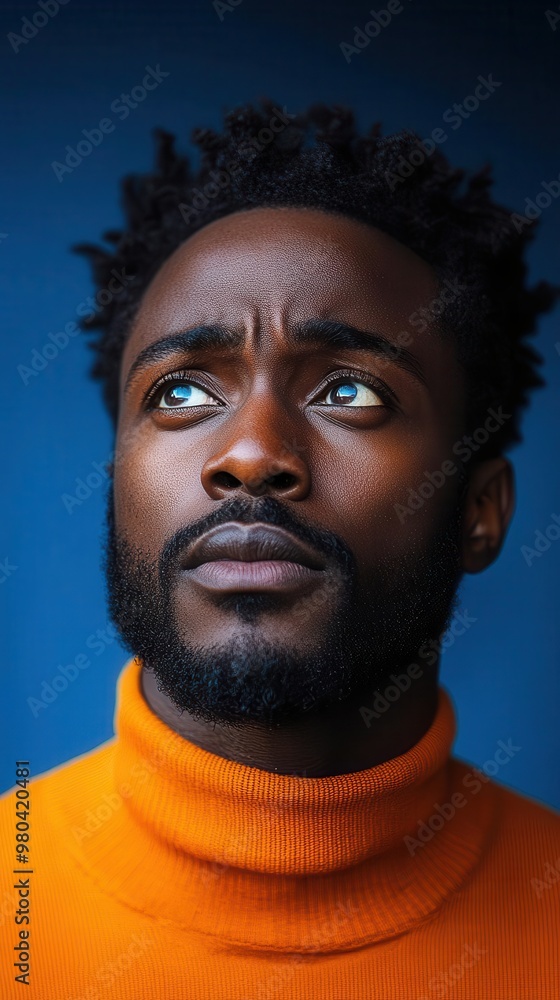 perplexed african man in vibrant orange top expressive facial features isolated against bold blue backdrop contemplative pose perplexed african man in vibrant orange top expressive facial features isolated against bold blue backdrop contemplative pose