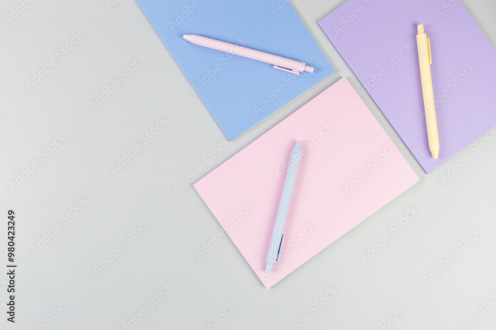 Top view of pink, purple and blue notebooks on grey background. Pink, yellow and blue pens, school, office wallpaper. Flat lay, copy space. Top view of pink, purple and blue notebooks on grey background. Pink, yellow and blue pens, school, office wallpaper. Flat lay, copy space.