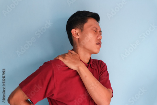 young asian man touching his shoulder with pain expression photo