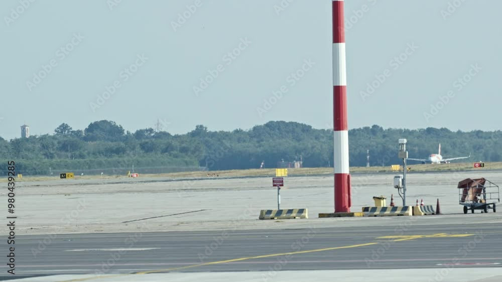 A plane is seen taxiing on an airport runway with a striped pole in the foreground A plane is seen taxiing on an airport runway with a striped pole in the foreground