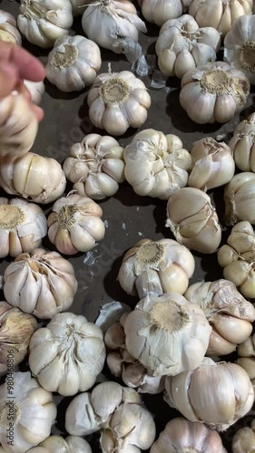 A person's hand selects a pile of garlic sold at a traditional market, the concept of shopping for cooking ingredients at the market