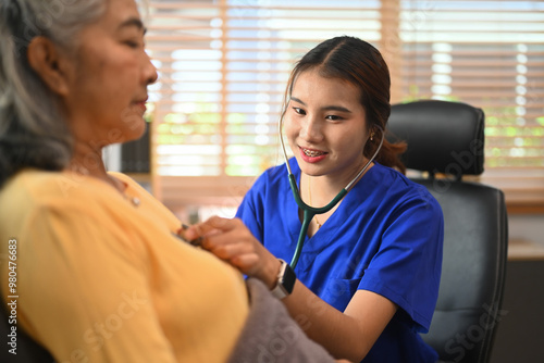 Female doctor in blue scrubs using a stethoscope examining elderly female patient