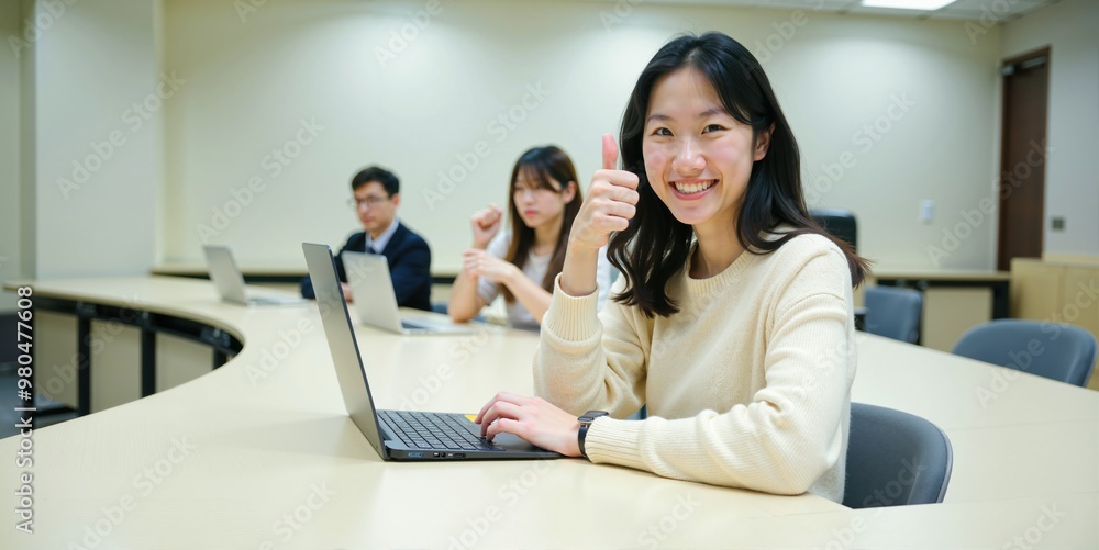 Asian Female Student Sitting in University Lecture Hall Using Laptop and Giving Thumbs Up Asian Female Student Sitting in University Lecture Hall Using Laptop and Giving Thumbs Up