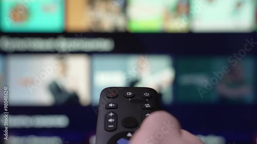 Person Browsing Streaming Services Using Remote Control. Hand Holding a Remote Control Browses Various Streaming Services On a Large Screen in a Comfortable Living Room Setting