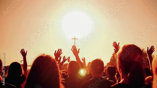 Silhouette of people with their arms raised during sunset with a cross in the background.