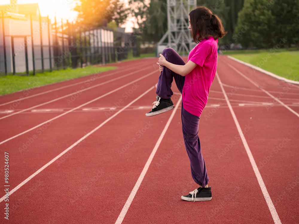 Young teenager girl doing stretches on a running track before run work out. Sport and healthy life style. Selective focus. Athletic routine in a public park fitness area. Young teenager girl doing stretches on a running track before run work out. Sport and healthy life style. Selective focus. Athletic routine in a public park fitness area.