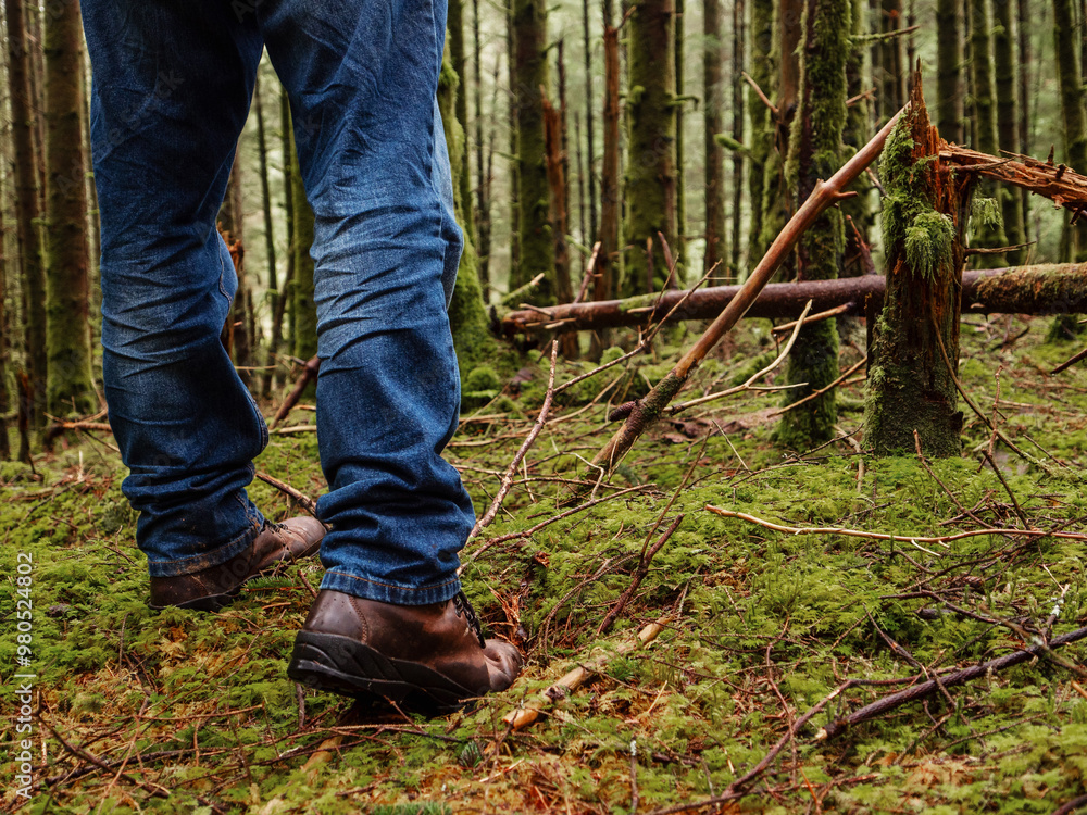 Tourist in blue jeans and tough brown leather outdoor boots on a green moss in a dense forest. Trip to nature and outdoor activity concept. Tourist in blue jeans and tough brown leather outdoor boots on a green moss in a dense forest. Trip to nature and outdoor activity concept.