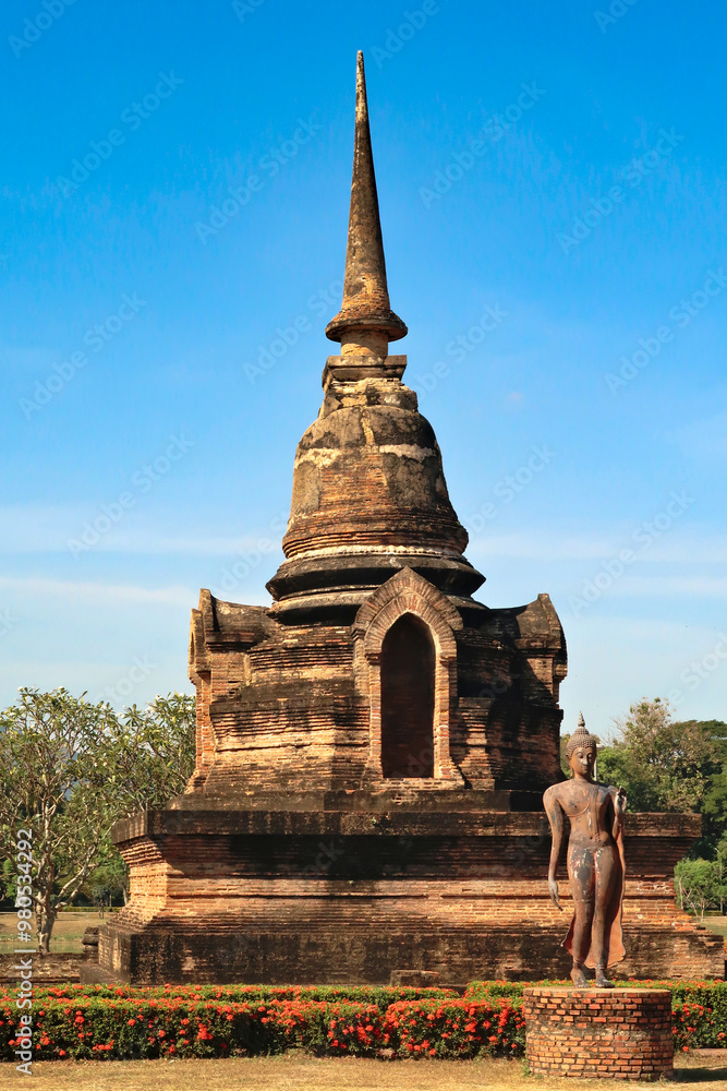 Fototapeta premium Standing buddha statue in front of a small pagoda next to the Wat Sa Si, Wat Sra Sri Temple at the Historical Park, the archaeological site, ancient ruins of Sukhothai, Thailand