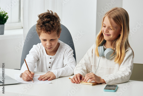 Happy Caucasian boy and girl studying together at home, using laptops and headphones for online elearning They are sitting at a table in the living room, fully concentrated on their studies Technology