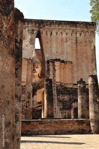 Catching a glimpse of the Phra Achana, a big sitting buddha statue inside of the Wat Si Chum Temple, Historical Park, archaeological site, ancient ruins of Sukhothai, Thailand photo