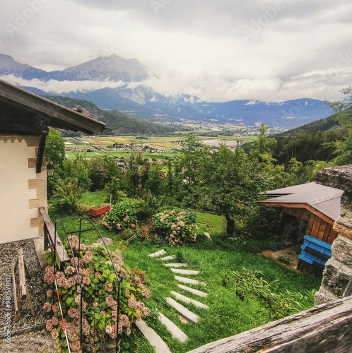 Vibrant, rustic view of an Alpine house in Rietz, Austria, overlooking lush green fields and mountains under a cloudy sky with vintage texture that adds an authentic, old feel to the scene. photo