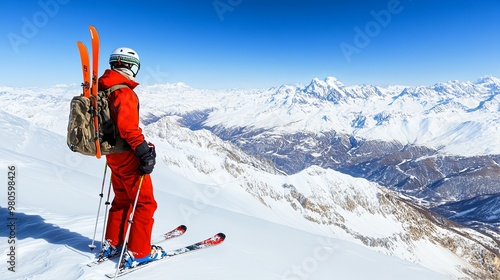 A skier in red gear stands on a snowy mountain peak, gazing at the breathtaking landscape under a clear blue sky.