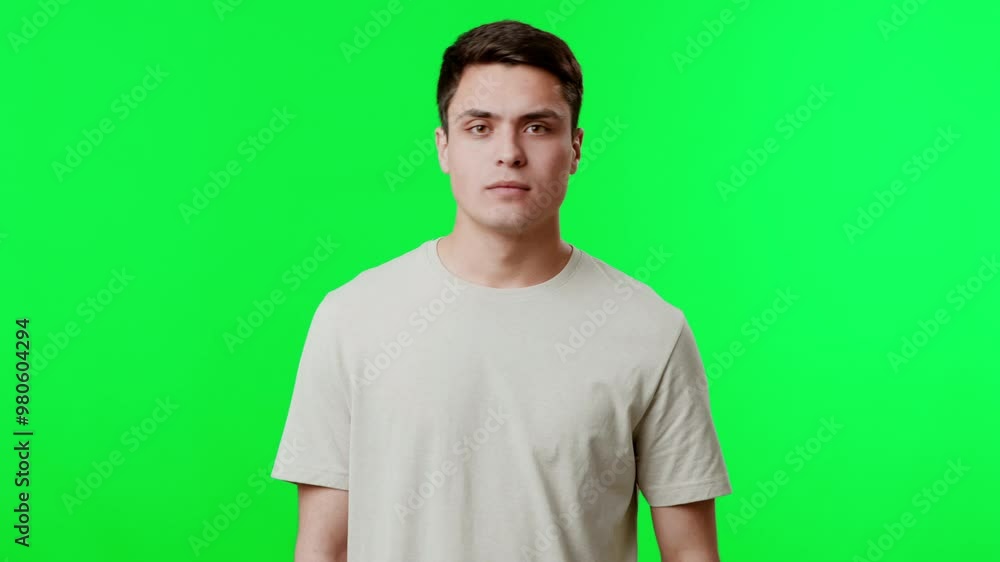 A young man stands confidently against a vivid green backdrop, displaying a neutral expression. His simple t-shirt and focused gaze suggest a candid moment ready for creative use. A young man stands confidently against a vivid green backdrop, displaying a neutral expression. His simple t-shirt and focused gaze suggest a candid moment ready for creative use.