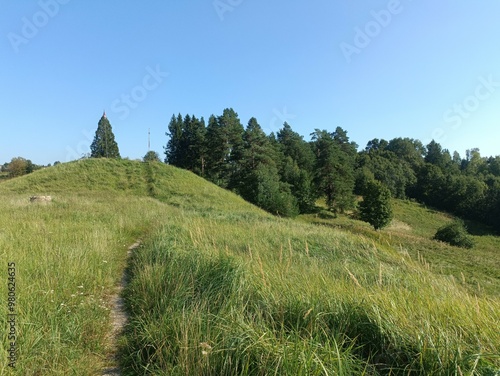 Bubiai hill during sunny day. Small hill. Grass is growing on hill. Staircase leading to the top. Sunny day with white and gray clouds in sky. Nature. Bubiu piliakalnis.	
 photo