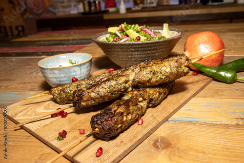 A delicious pile of three Spiced Lamb Kaftas kababs with a bowl of salad and pomegranate seeds on a wooden kitchen work top photo