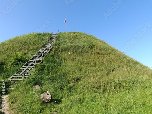 Bubiai hill during sunny day. Small hill. Grass is growing on hill. Staircase leading to the top. Sunny day with white and gray clouds in sky. Nature. Bubiu piliakalnis.	
 photo