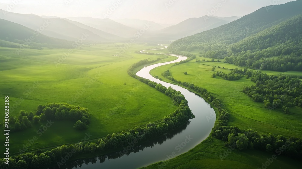 This image showcases a serene aerial view of a winding river cutting through lush, green fields, with mist-covered mountains in the distance. This image showcases a serene aerial view of a winding river cutting through lush, green fields, with mist-covered mountains in the distance.