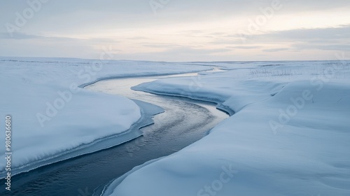 A small river winding through a snow-covered landscape, with ice forming along the banks under a pale winter sky.