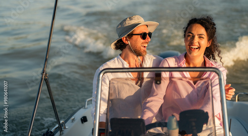 A happy couple enjoying a boat ride on a sunny day, with the man wearing a hat and sunglasses and the woman laughing. photo