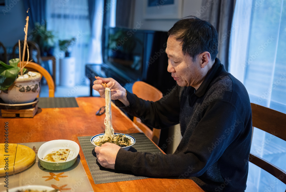 Man eating noodles with chopsticks at home.