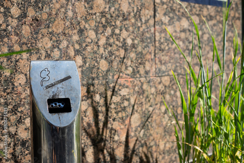 Modern ashtray on street in smoking area, metal pole with compartment for disposing of cigarettes, health problems of smoking of the population people on city street in public place photo